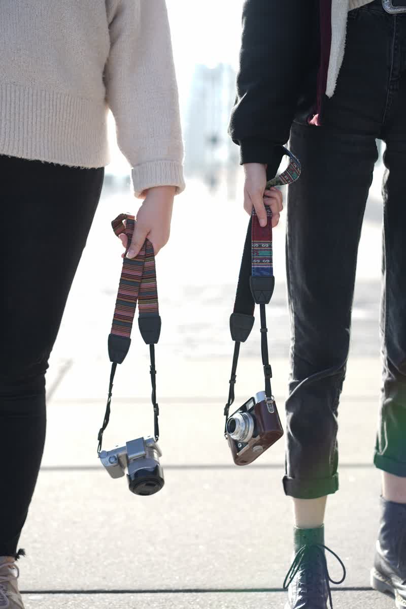 Zwei Mädchen mit Kameragurt in der Hand mit Gegenlicht fotografiert