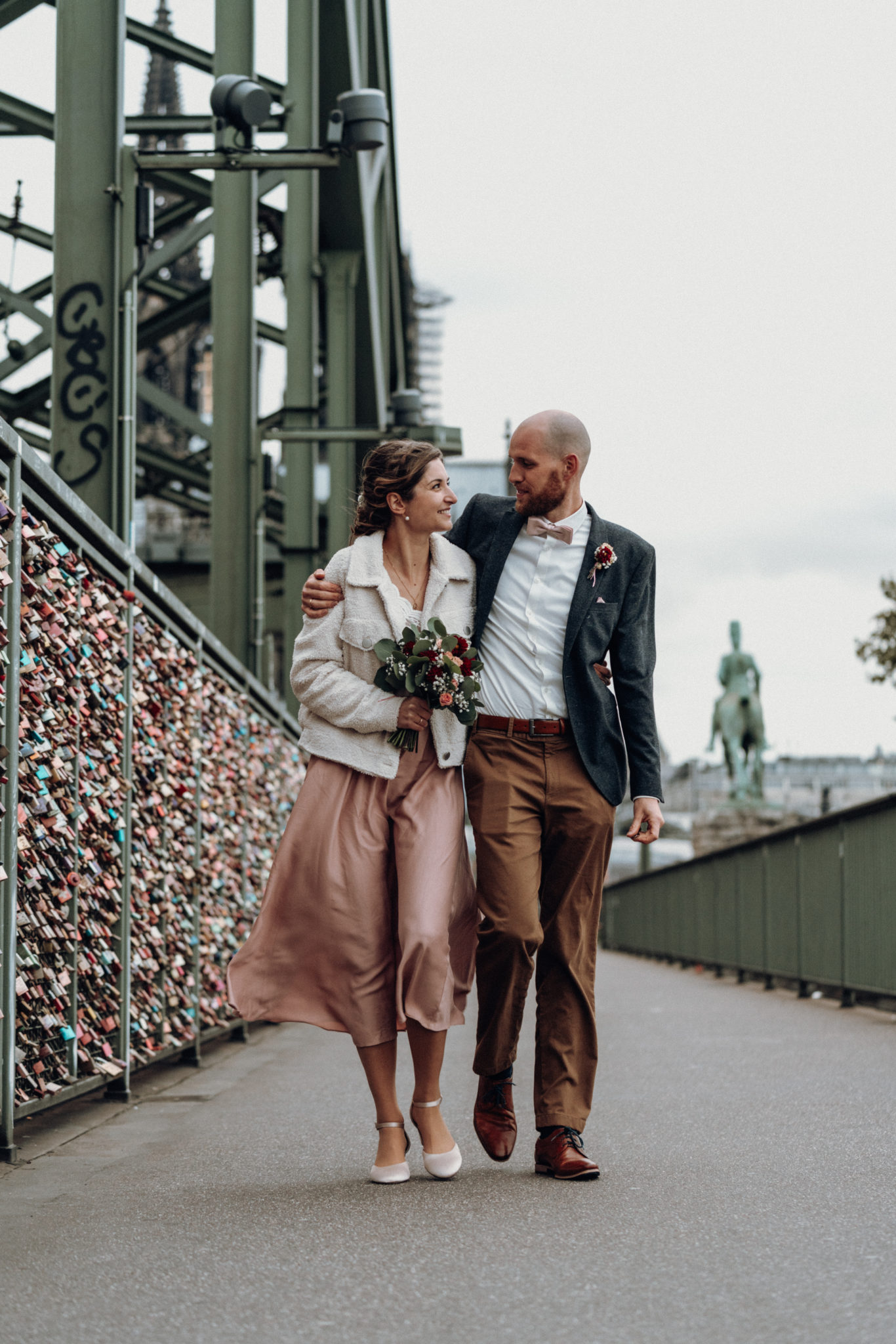 Hochzeitspaar läuft Arm in Arm sich anschauend über die Hohenzollernbrücke in Köln