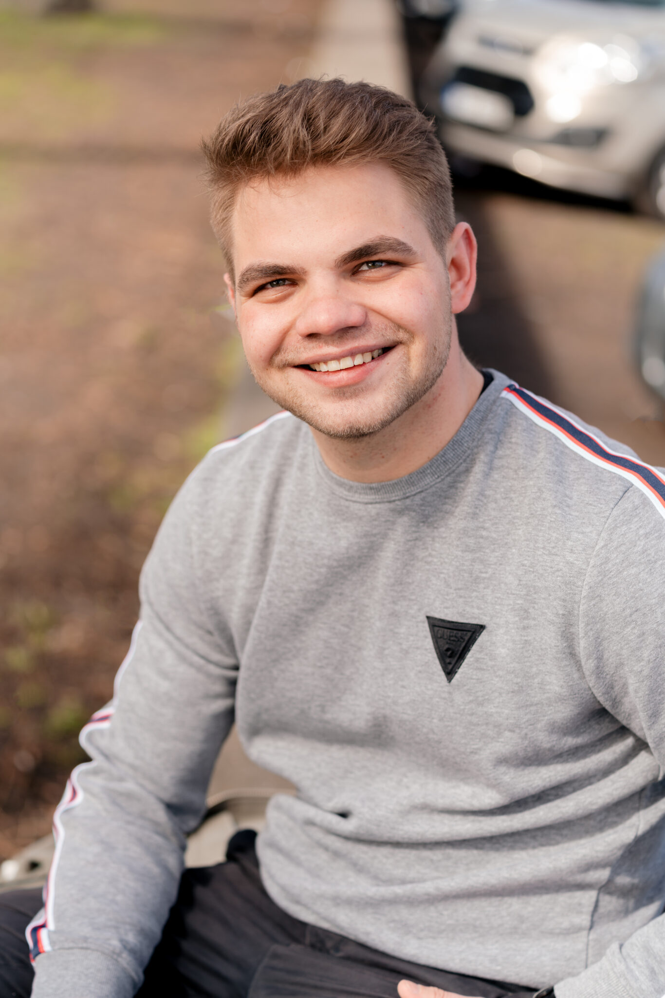 Junger Mann bei Tinder Fotoshooting sitzt auf einer mauer und lächelt