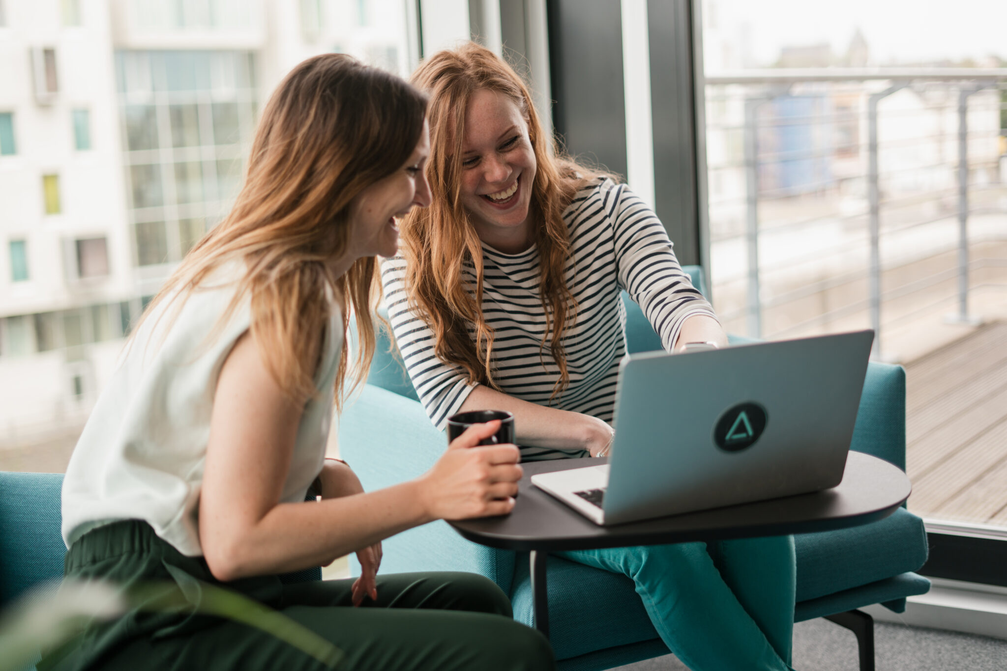 Zwei Frauen sitzen gemeinsam an einem Laptop und lachen