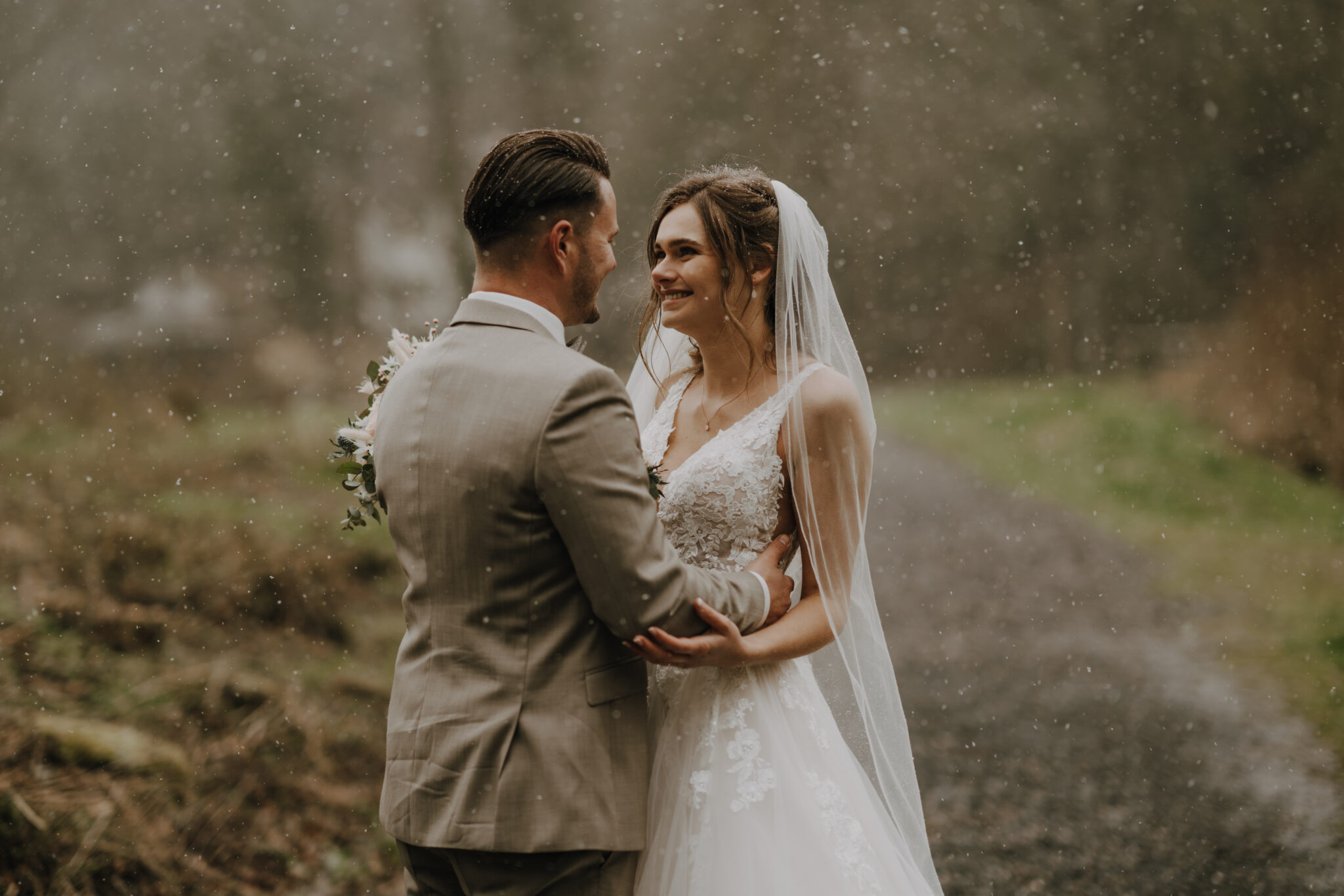 Hochzeitspaar steht beim Shooting lächelnd im Regen