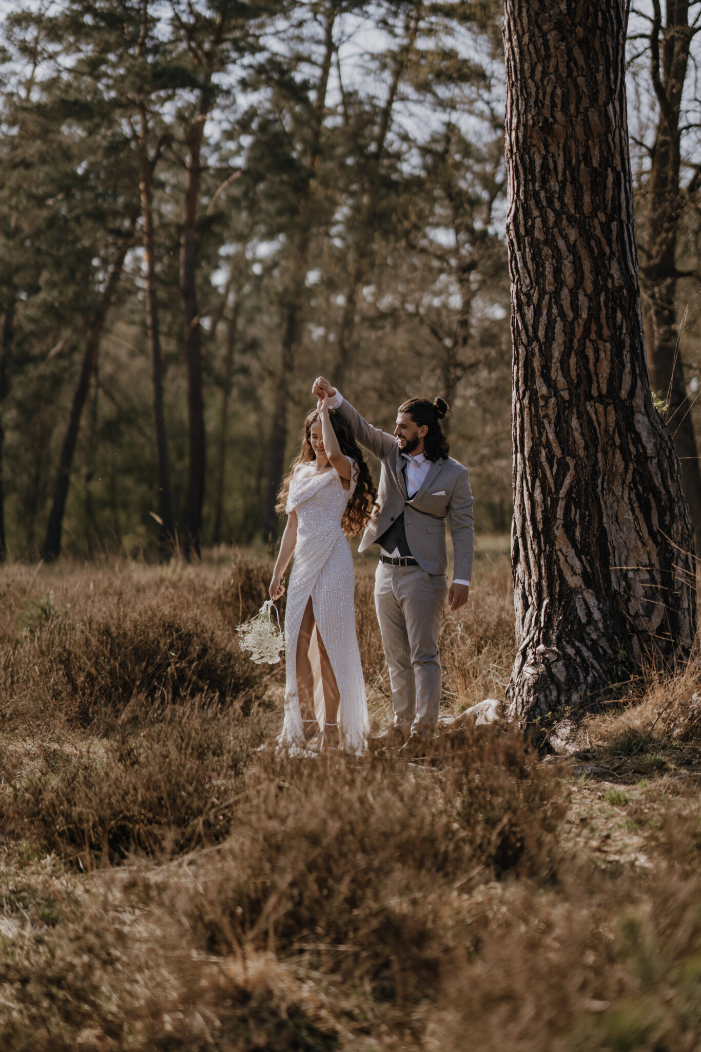 Das Brautpaar steht neben einem großen Kieferbaum und die Braut dreht sich in der Hand des Bräutigam 