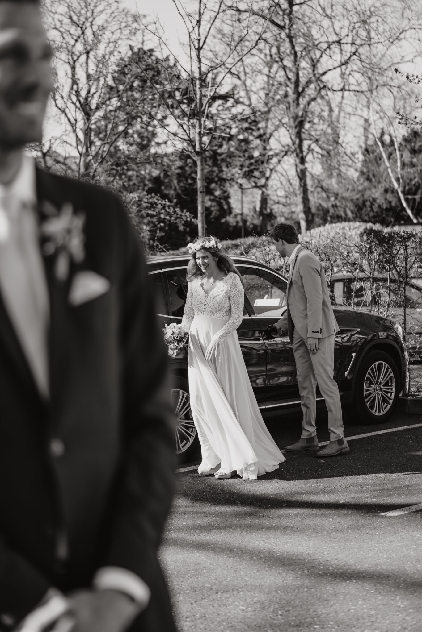Braut steigt lachend aus Auto, Boho-Kleid, Blumenkranz