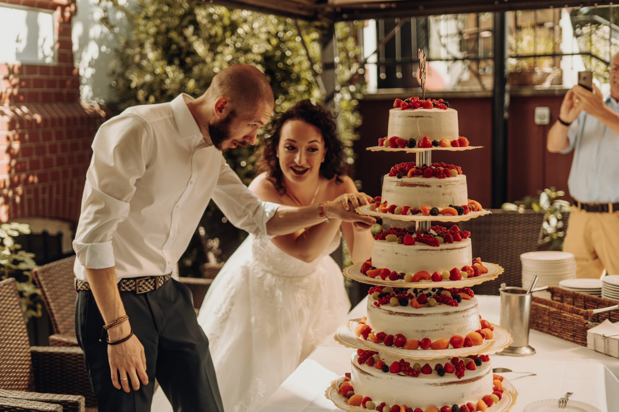 Brautpaar schneidet Hochzeitstorte an, Hochzeitsgesellschaft glücklich und klatscht