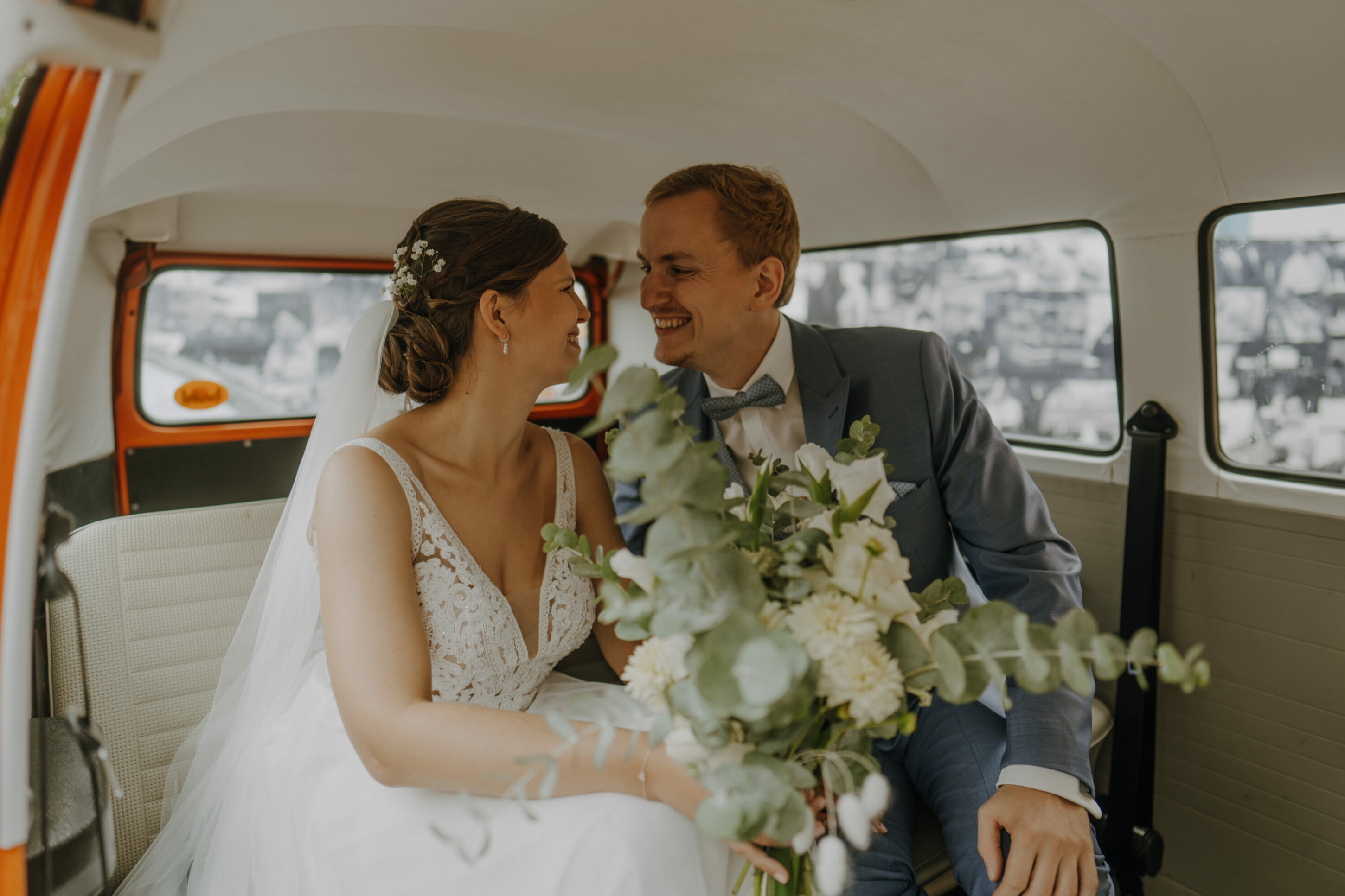 Hochzeitspaar sitzt glücklich in Hochzeitsauto, dem roten VW Bulli 