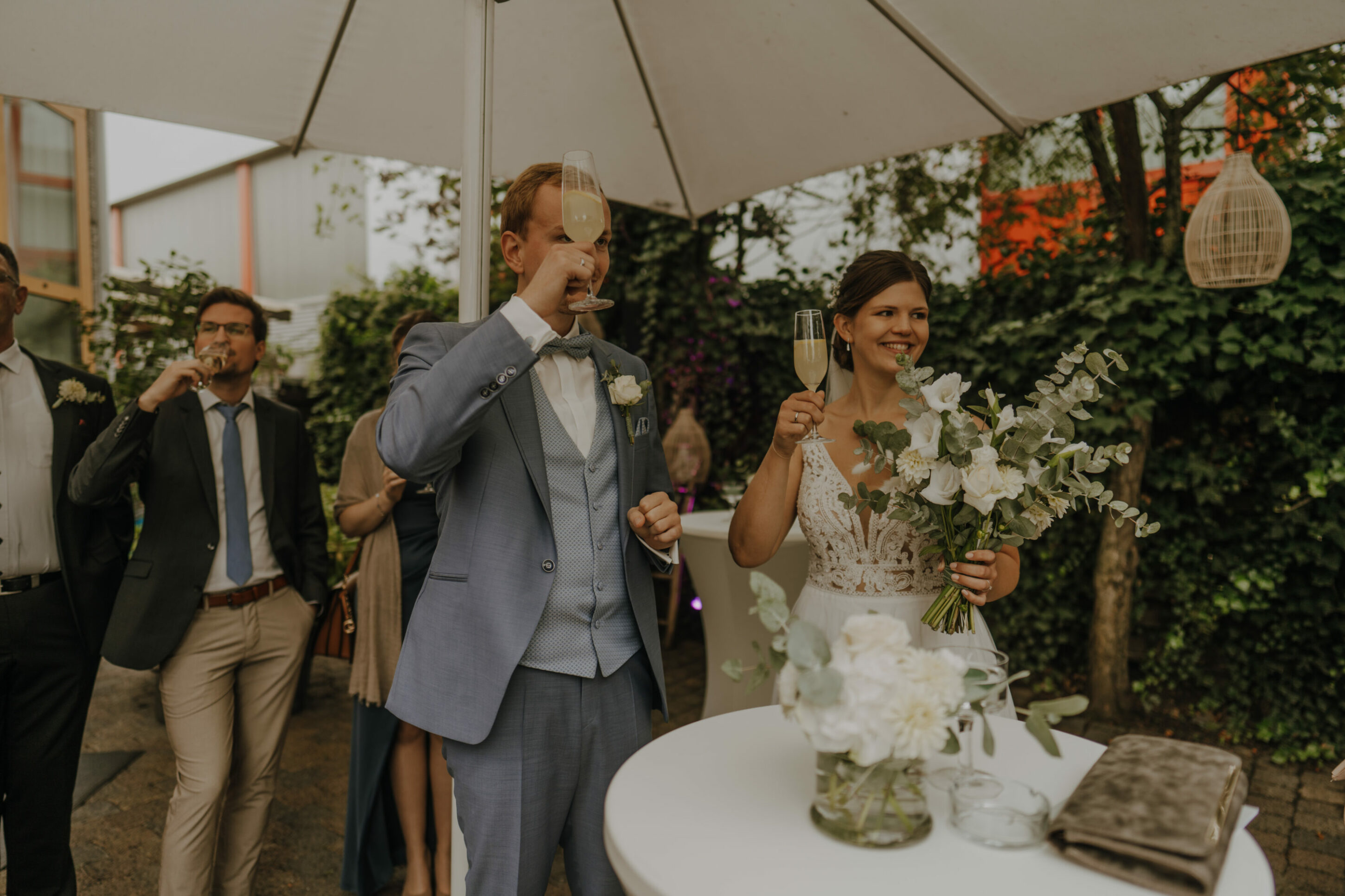 Hochzeitsgesellschaft stößt mit Sekt auf Brautpaar an, alle lachen und sind glücklich