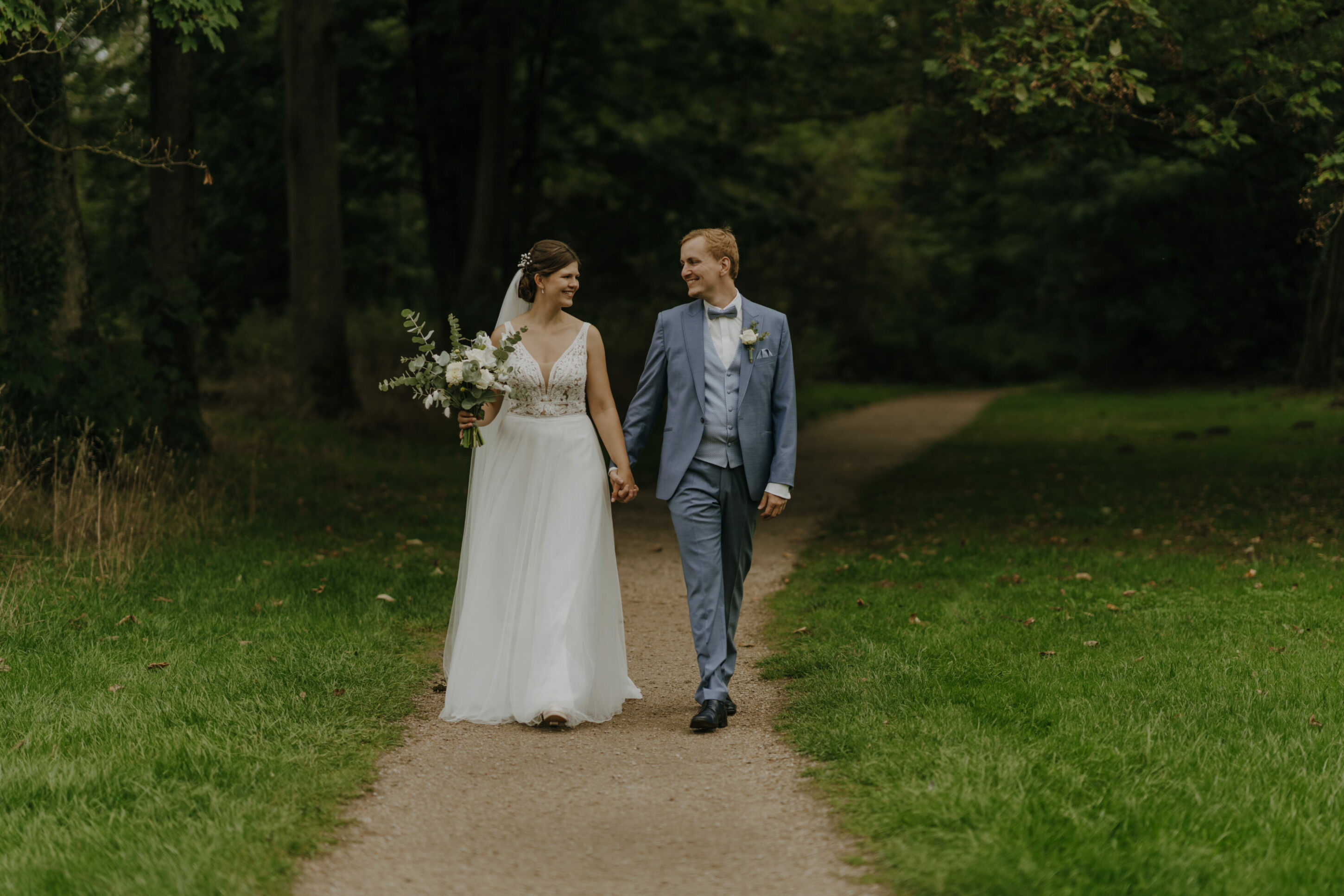 Hochzeitsfotoshooting auf Wiese beim Schloss Falkenlust, Brautpaar geht Hand in Hand