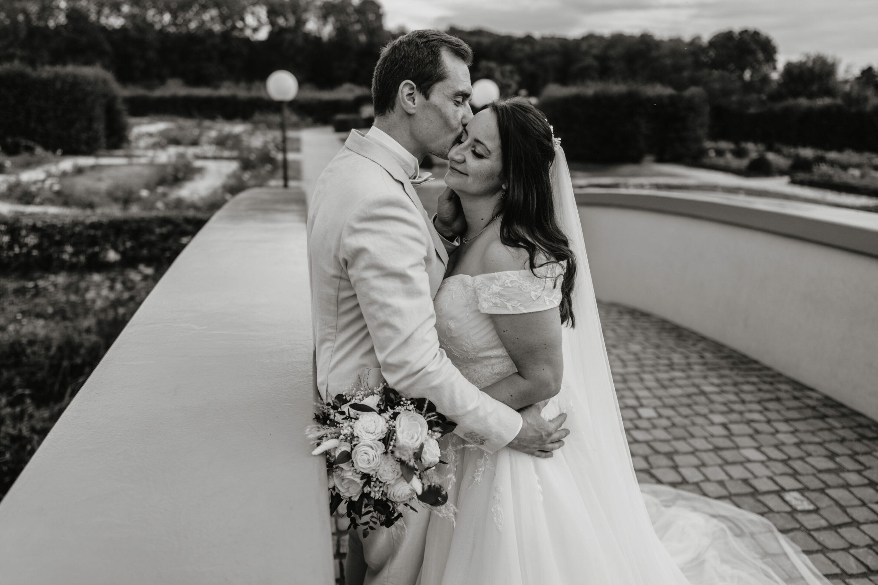 Brautpaar auf Brücke, Bräutigam küsst Braut auf Schläfe, nahe Aufnahme, schwarz-weiß