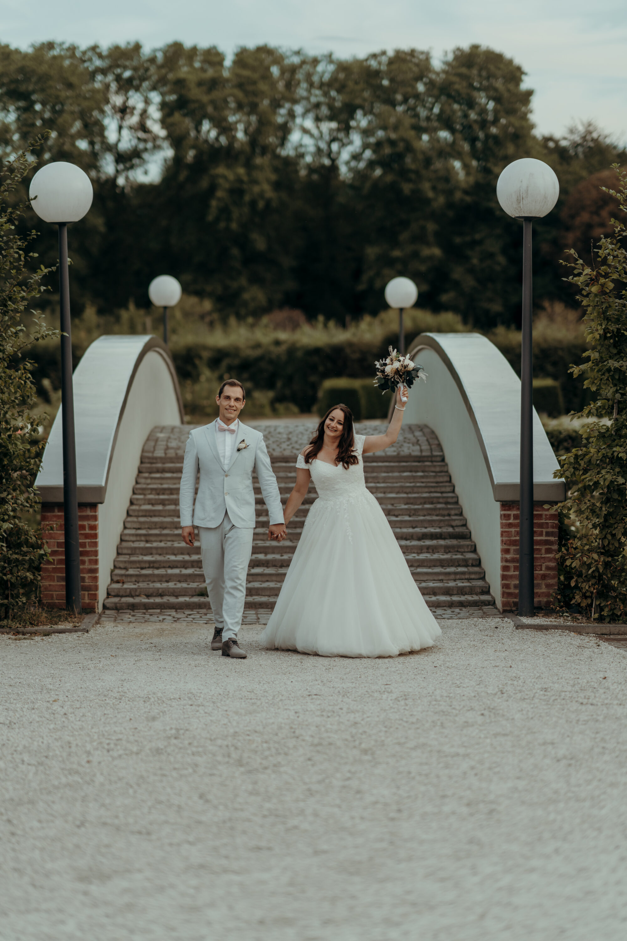 Brautpaar vor Brücke mit großen Laternen, auf Kamera zulaufend, Braut hält Strauß hoch