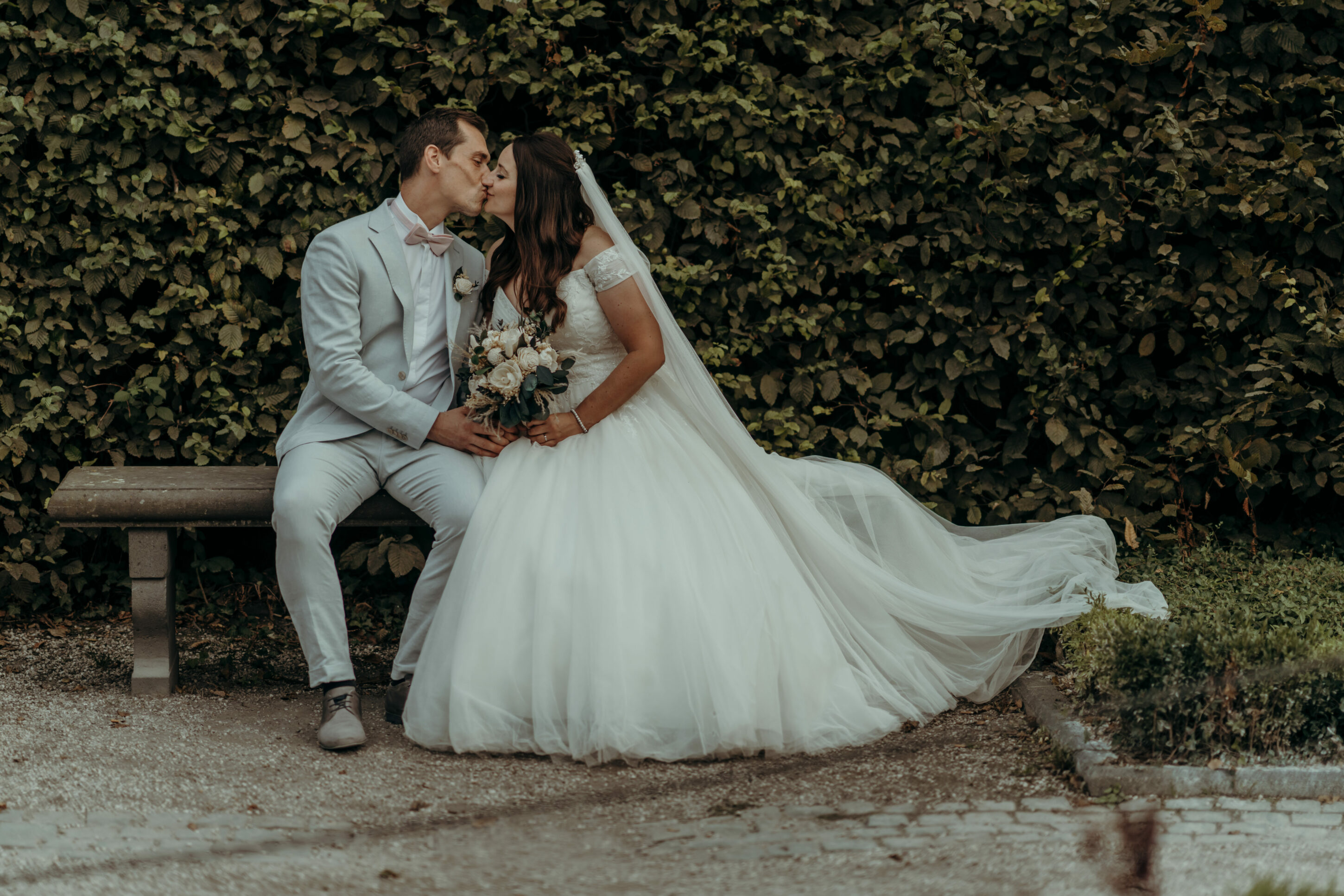 Brautpaar sich küssend auf Schlossbank vor Hecke