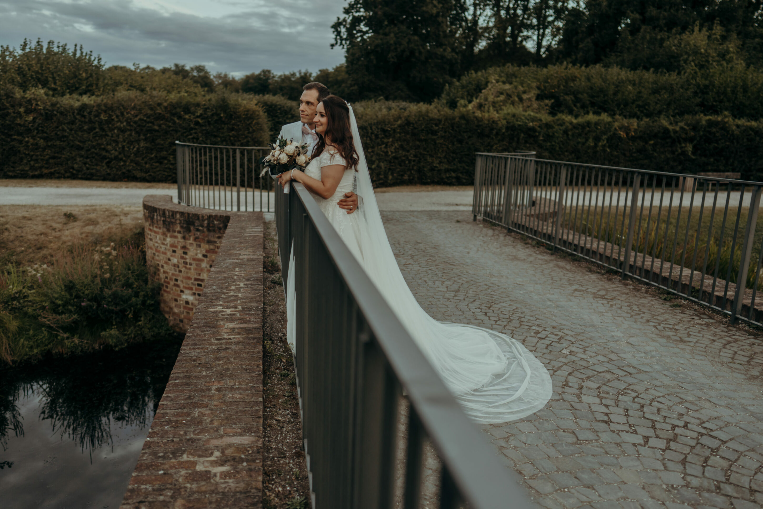 Brautpaar auf kleiner Brücke, in die Ferne schauend an Geländer