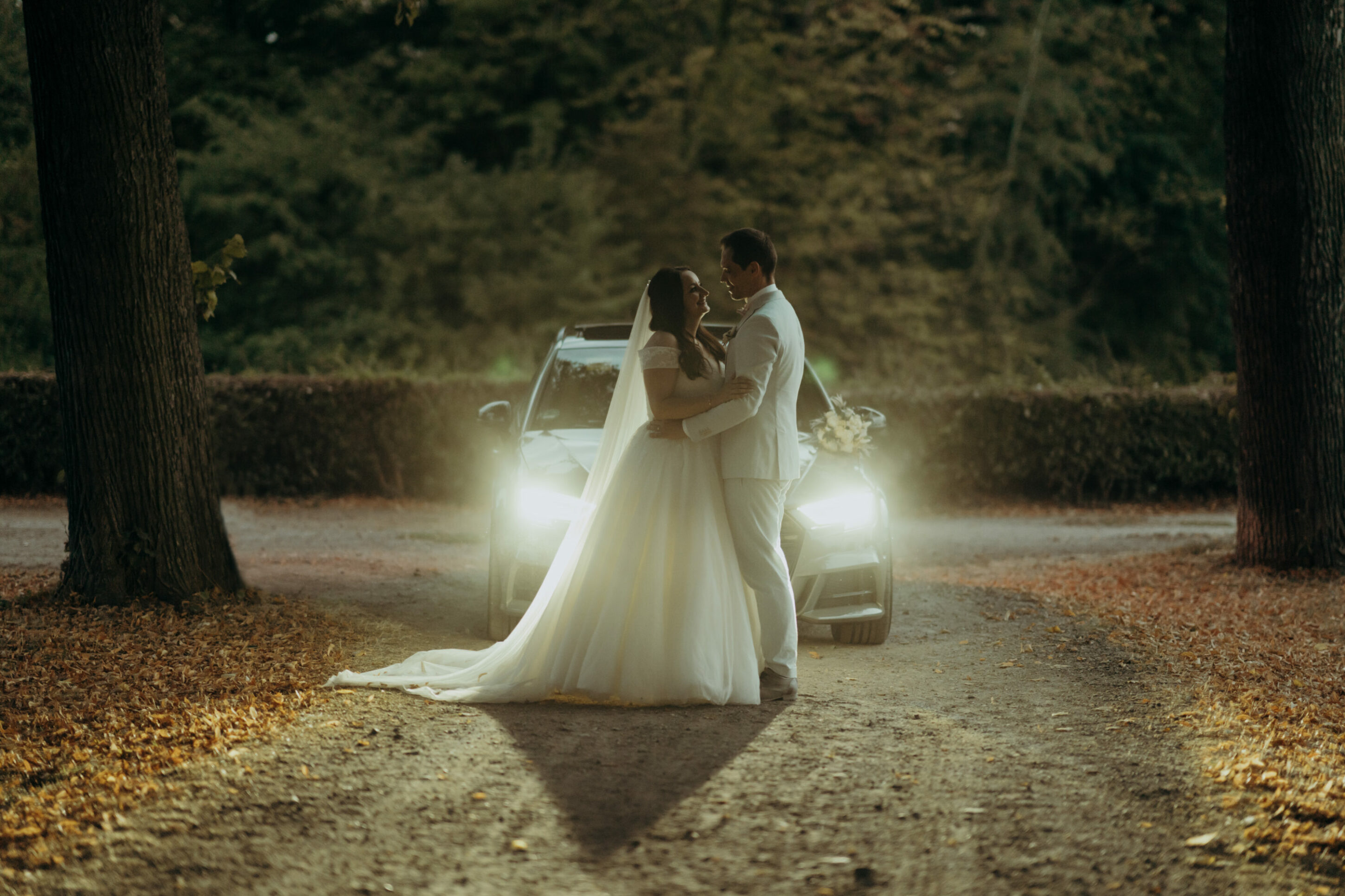Brautpaar in Dämmerung vor Autoscheinwerfern sich in die Augen schauend