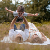 Familienfotoshooting, Eltern, die mit ihrem Sohn den Flieger machen, während sie in der Wahner Heide auf dem Boden liegen.