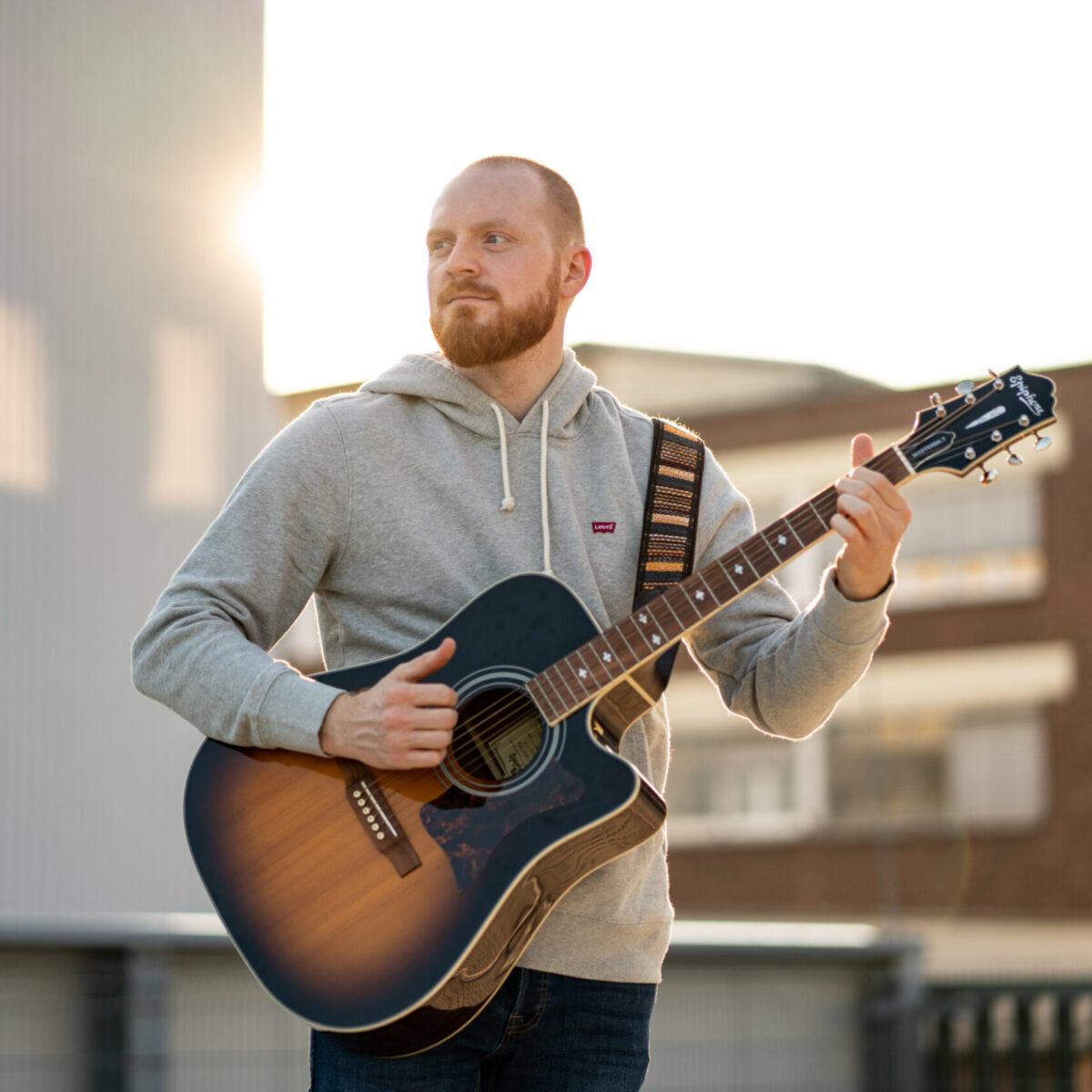 Fotoshooting für Online-Dating Tinder & Co.ist die beste Lösung, sich selber zu präsentieren. Hier auf dem Bild hält ein Ann seine Gitarre in der Hand bei warmer, oranger Abendsonne.