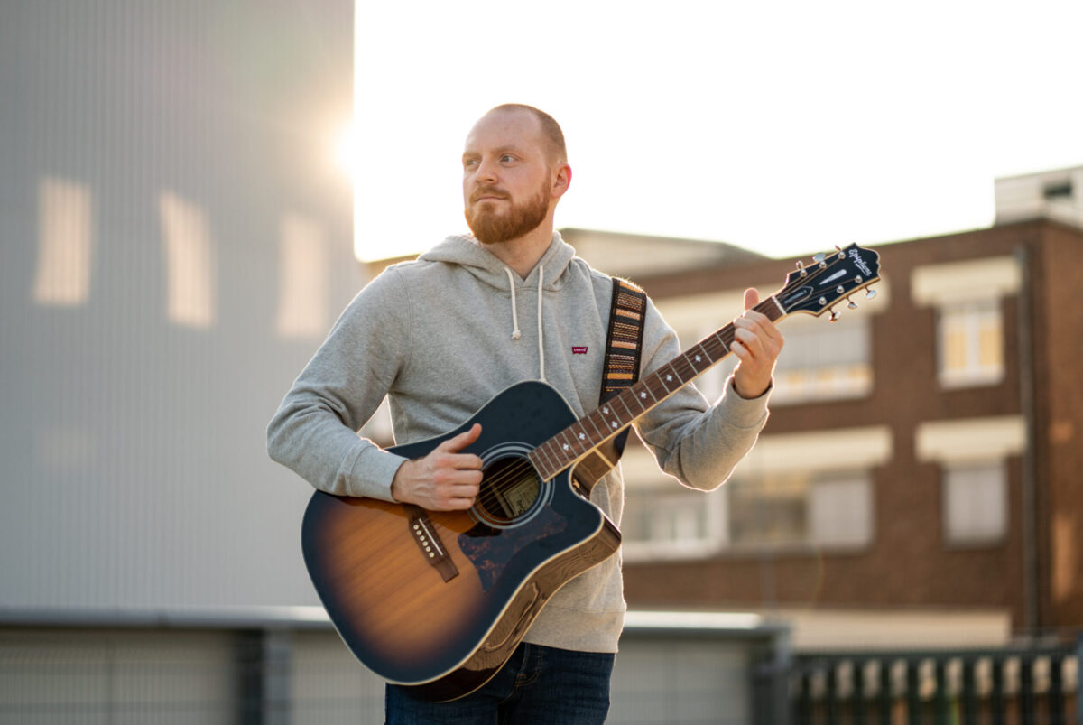 Fotoshooting für Online-Dating Tinder & Co.ist die beste Lösung, sich selber zu präsentieren. Hier auf dem Bild hält ein Ann seine Gitarre in der Hand bei warmer, oranger Abendsonne.