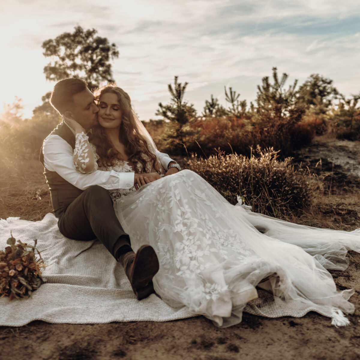 After Wedding Fotoshooting in der Wahner Heide bei Abendsonne. Das Paar in ihren Hochzeitsoutfits, um die Magie des Tages und die Liebe zueinander nochmal aufleben zu lassen und durch Bilder, im sitzen auf einer Decke, festzuhalten.