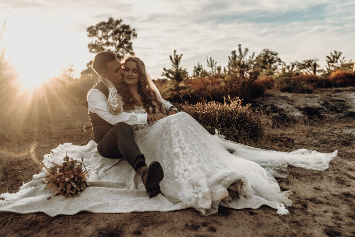 After Wedding Fotoshooting in der Wahner Heide bei Abendsonne. Das Paar in ihren Hochzeitsoutfits, um die Magie des Tages und die Liebe zueinander nochmal aufleben zu lassen und durch Bilder, im sitzen auf einer Decke, festzuhalten.