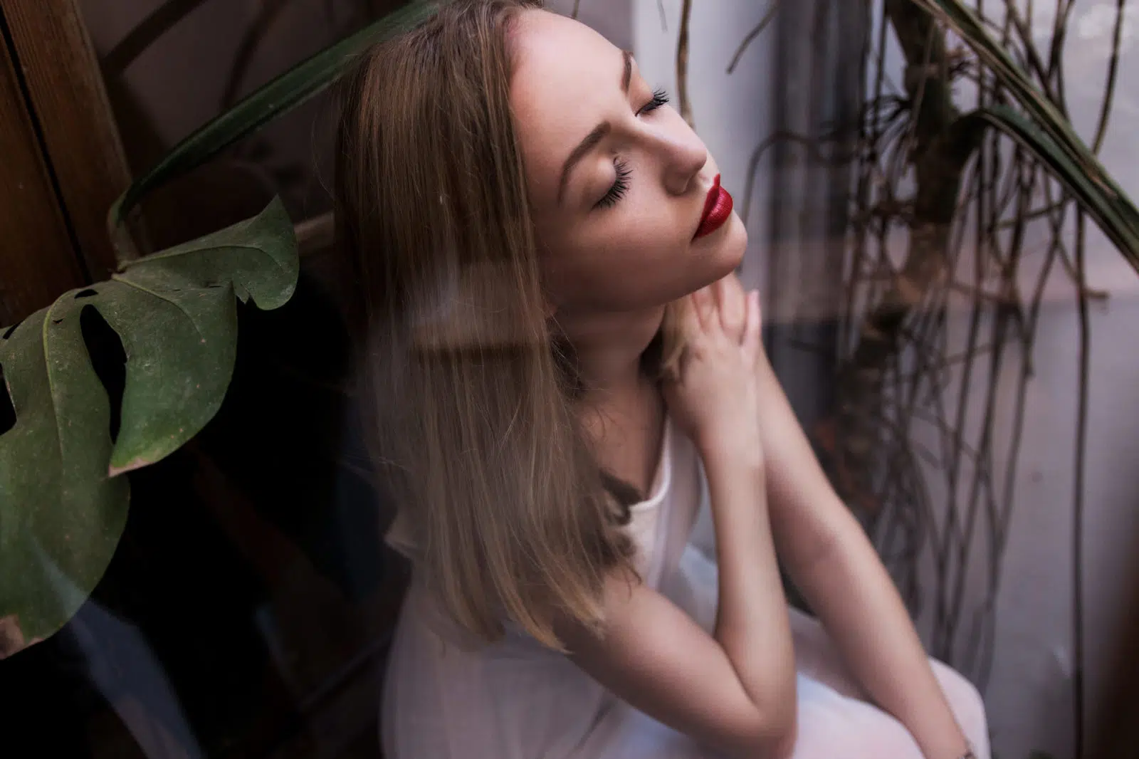 Portraitfoto einer Frau mit geschlossenen Augen, sitzend am Fenster