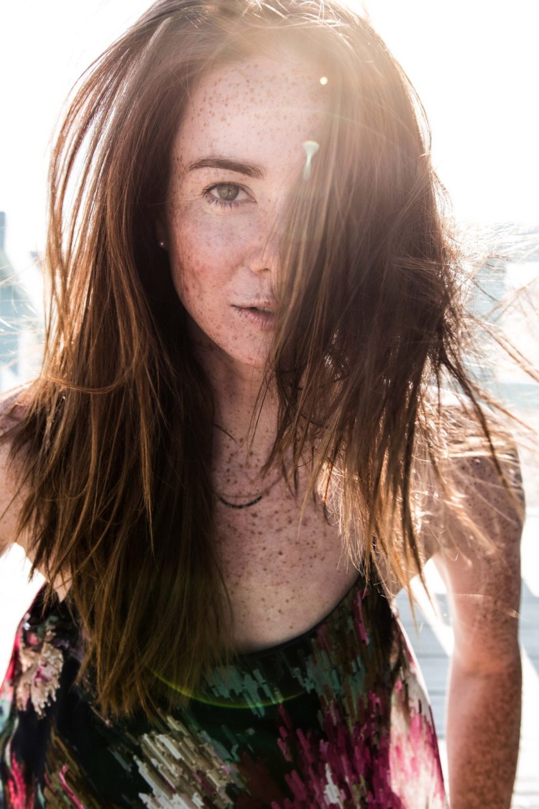 Natürliches Portraitfoto einer Frau, Haare wehen in ihr Gesicht, während die Sonne von hinten scheint
