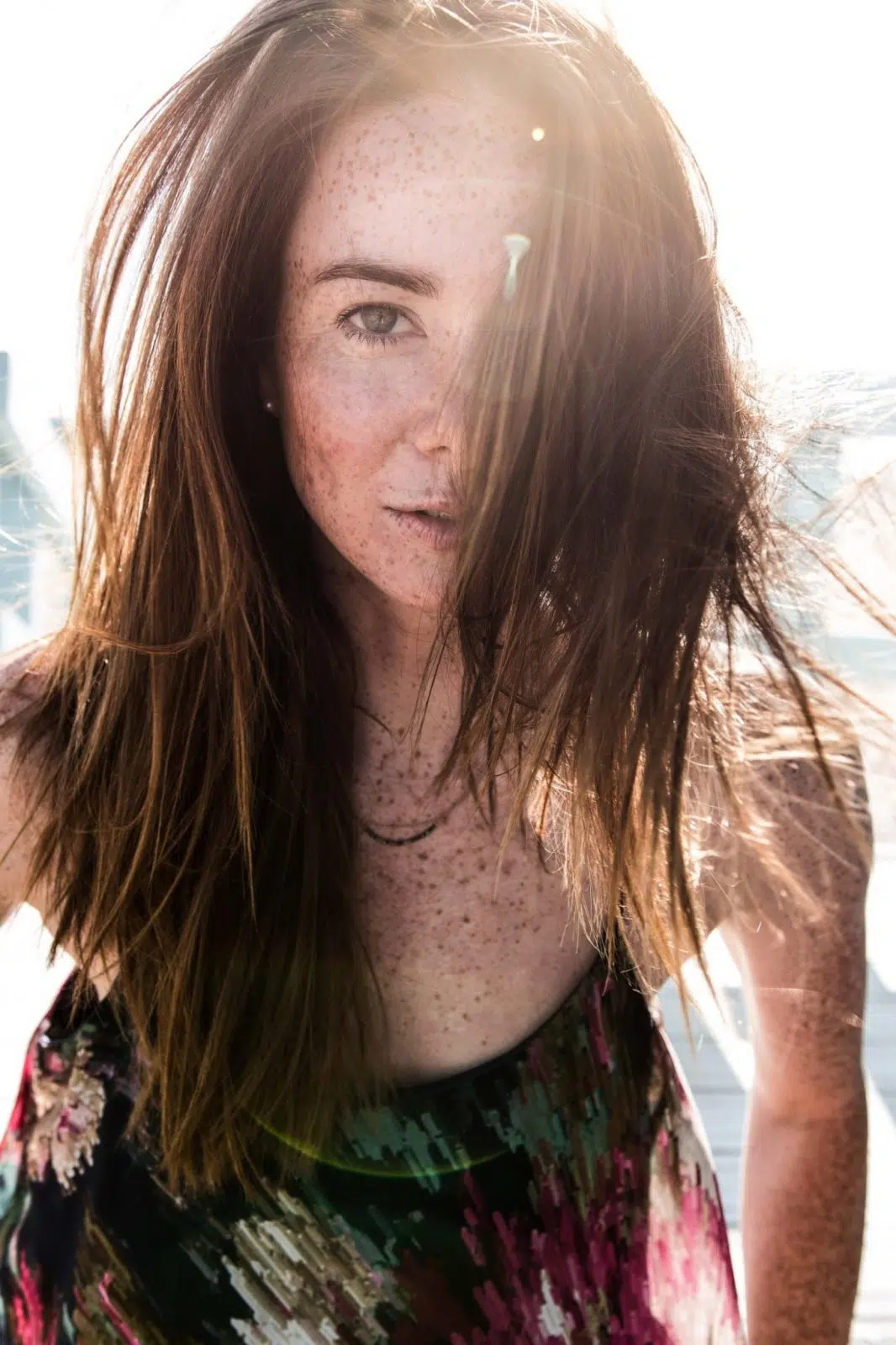 Natürliches Portraitfoto einer Frau, Haare wehen in ihr Gesicht, während die Sonne von hinten scheint