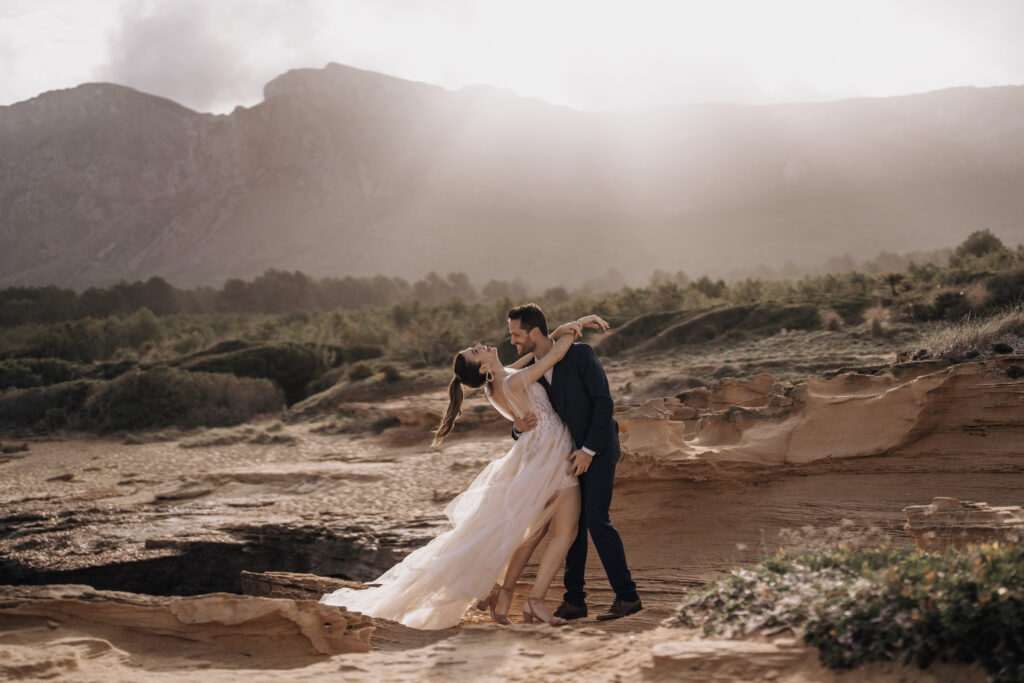 Hochzeitsportfolio, Braut und Bräutigam stehen eng umschlungen vor Bergen mit Gegenlicht