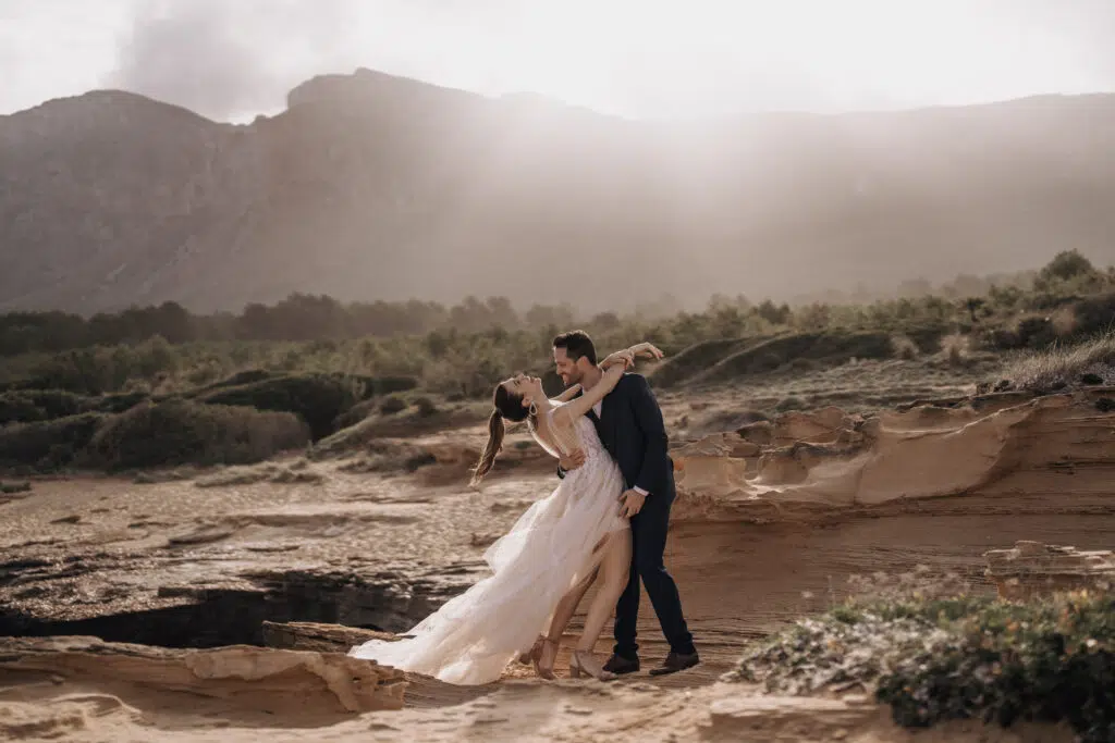 Hochzeitsportfolio, Braut und Bräutigam stehen eng umschlungen vor Bergen mit Gegenlicht