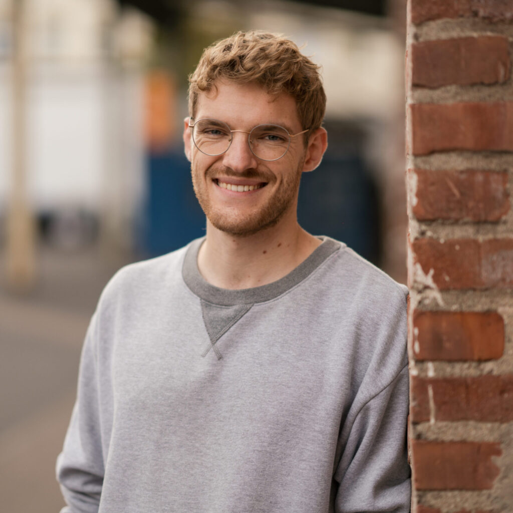 Freundliches Portraitfoto eines Mannes, der sich an eine Backsteinmauer anlehnt