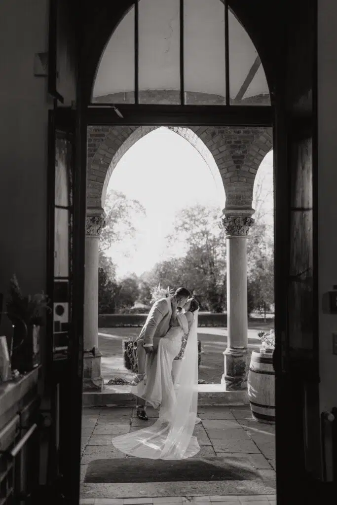 Hochzeitsportfolio, Hochzeitspaar unter einem steinerndem Torbogen, Gegenlichtaufnahme in Schwarz-Weiß