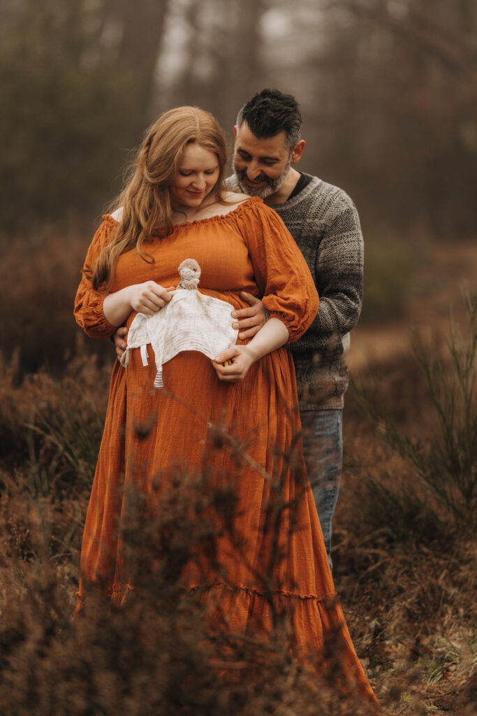Babybauch Fotografie Portfolio Paar steht in einem Feld und umarmt sich Frau trägt ein orangefarbenes langes Kleid