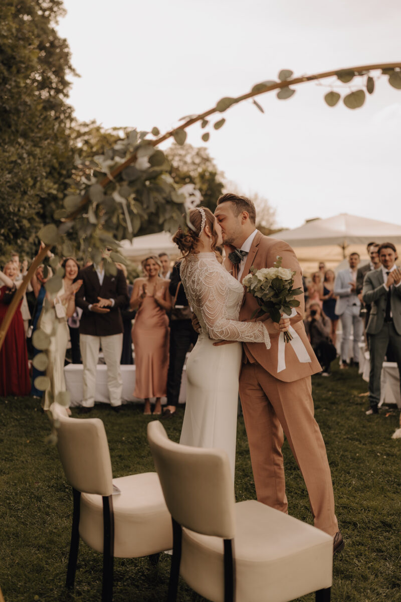 Hochzeitsportfolio, Brautpaar beim Hochzeitskuss im Hintergrund die Gäste am klatschen