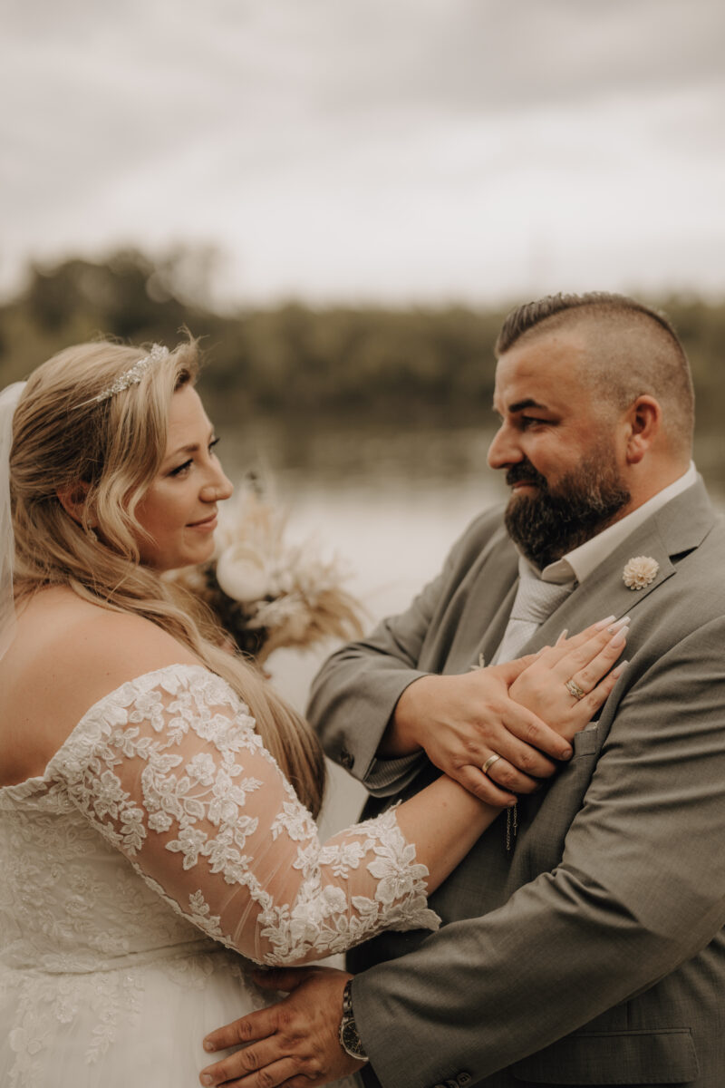 Brautpaar steht sich gegenüber und schaut sich an, die Hand der Braut auf der Brust des Bräutigams warm Hochformat