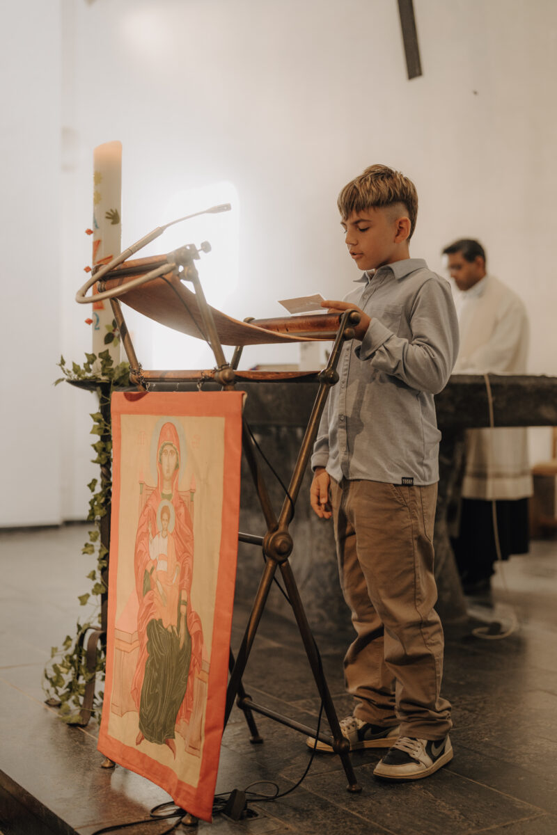 Junge im hellblauen Hemd steht am Pult und liest