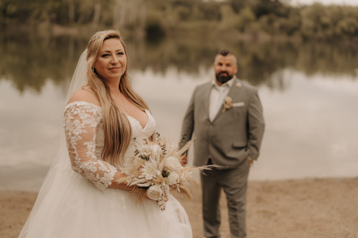 Bräutigam steh im Hintergrund unscharf, Braut imVordergrund scharf, warm, Querformat