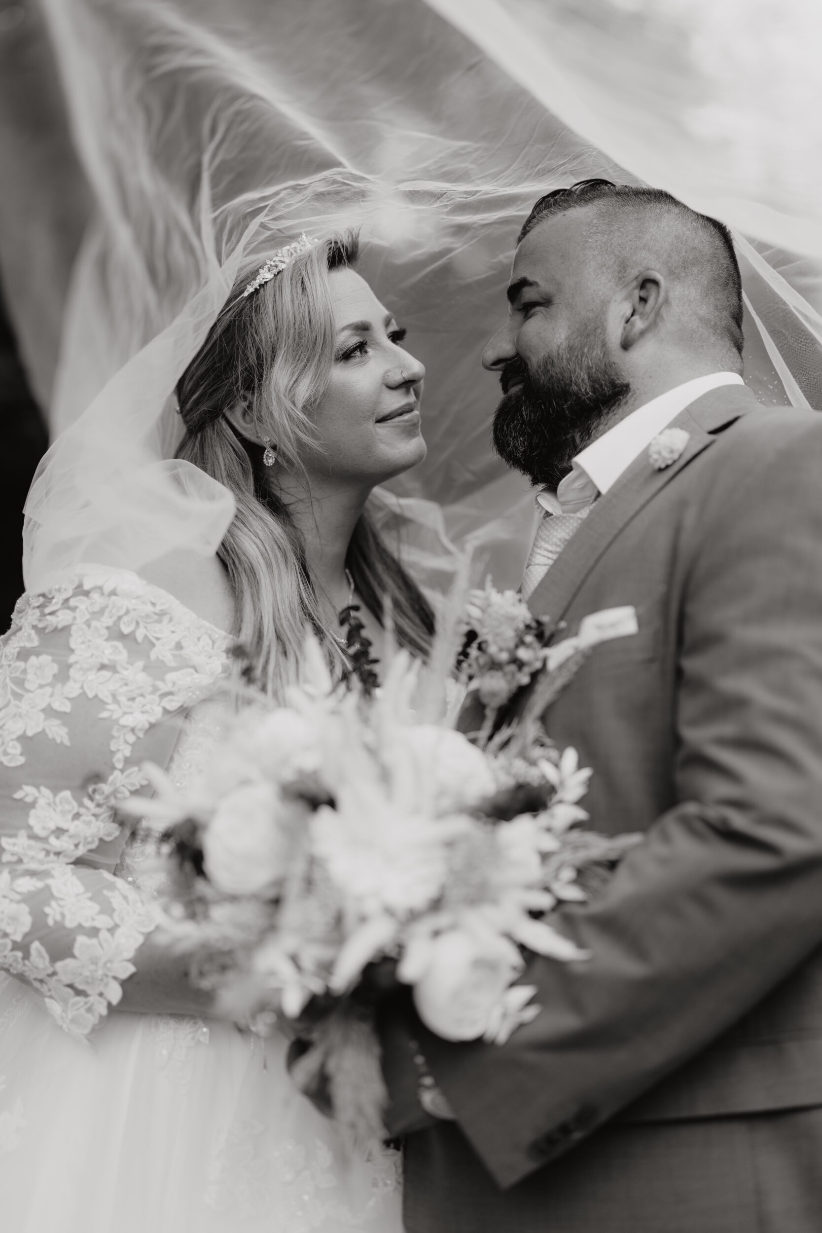 Foto Braut und Bräutigam sehen sich unter dem Schleier zärtlich an Hochformat schwarz weiß