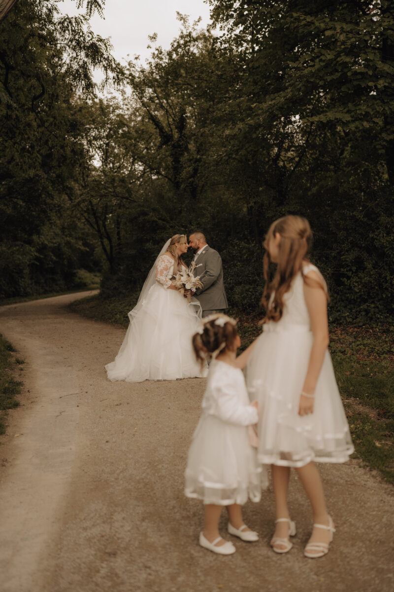 Kinder vorne, schauen nach hinten zum Brautpaar, das sich küsst, Wald im Hintergrund, Hochformat warm