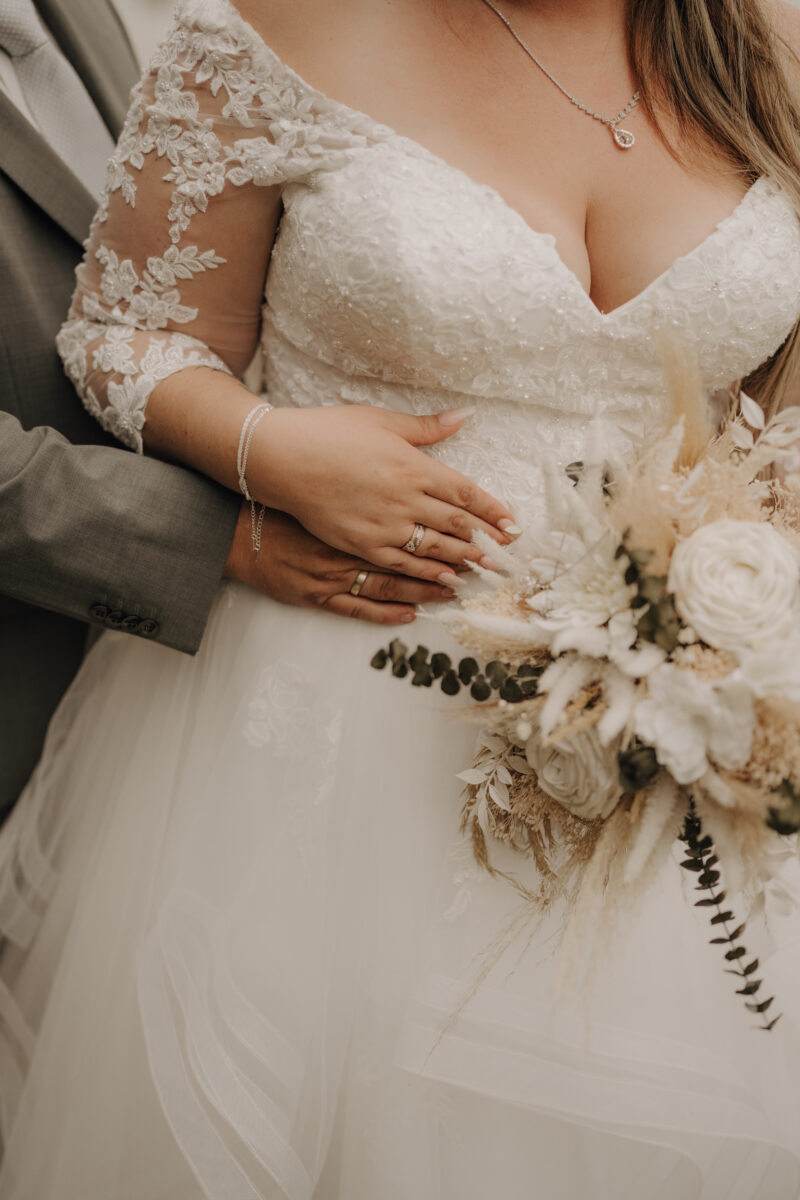 Foto Brautkleid, Hände vom Brautpaar auf dem Kleid übereinander gelegt und Brautstrauß der rechten Seite warm Hochformat