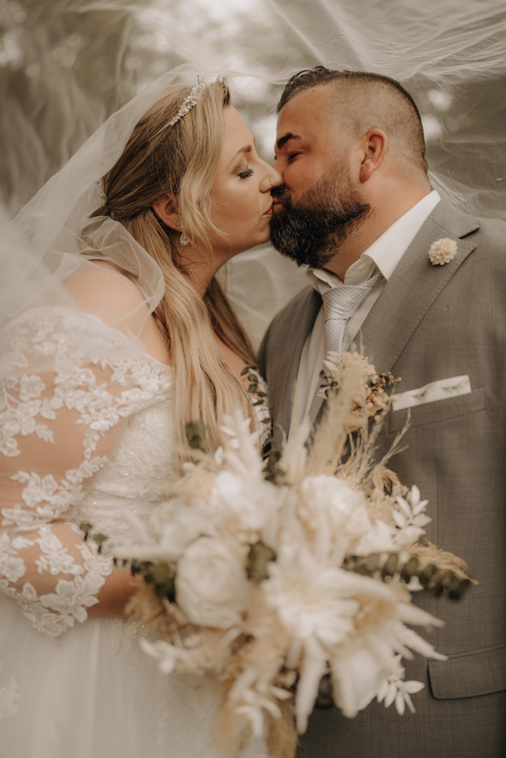 Foto Brautpaar küsst sich unter dem Schleier halbnah warm Hochformat