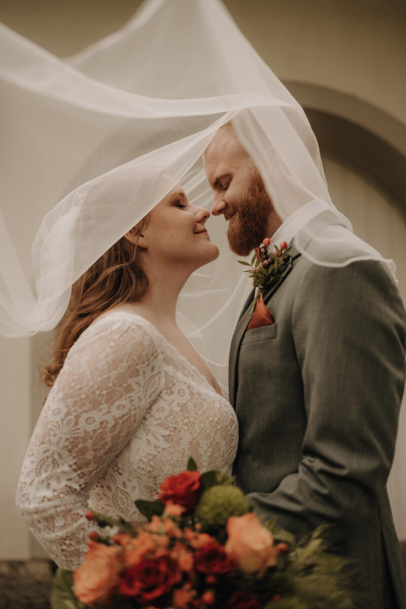 hochzeitsportfolio, hochzeitspaar nah aneinander nasenspitze an nasenspitze, augen geschlossen, schleier der Braut über die beiden