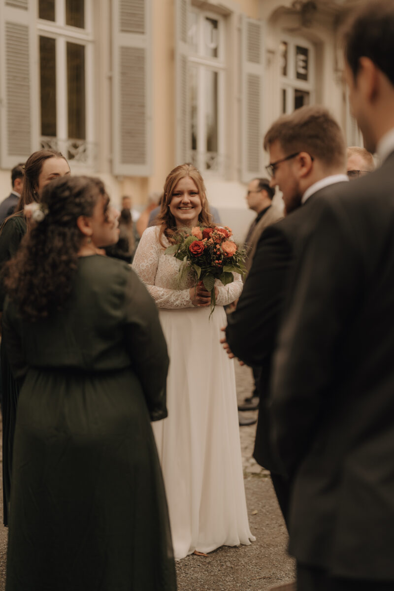Braut steht mit Strauß zwischen den Gästen