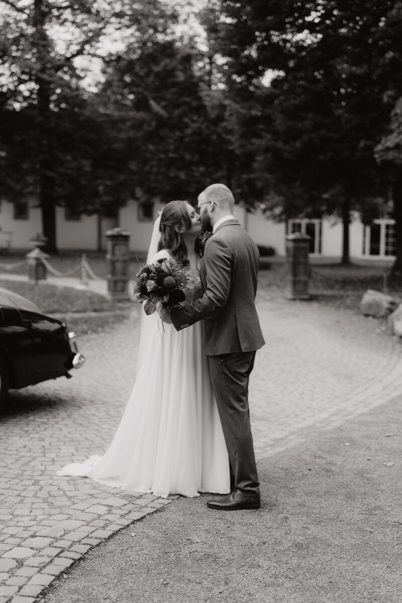 Hochzeitsportfolio, Braut und Bräutigam stehen nah beieinander, küssen sich gegenseitig, bild in Schwarz Weiß