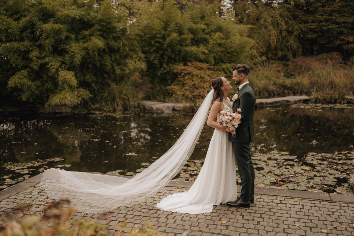 Hochzeitsportfolio, Braut und Bräutigam stehen nah gegenüber vor einem Teich auf einem Weg davor