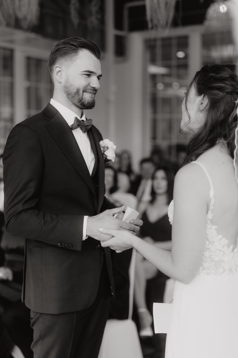 Hochzeitsportfolio, Braut und Bräutigam schauen sich verliebt an, Braut hält die Hand des Bräutigams fest, Bild in Schwarz Weiß