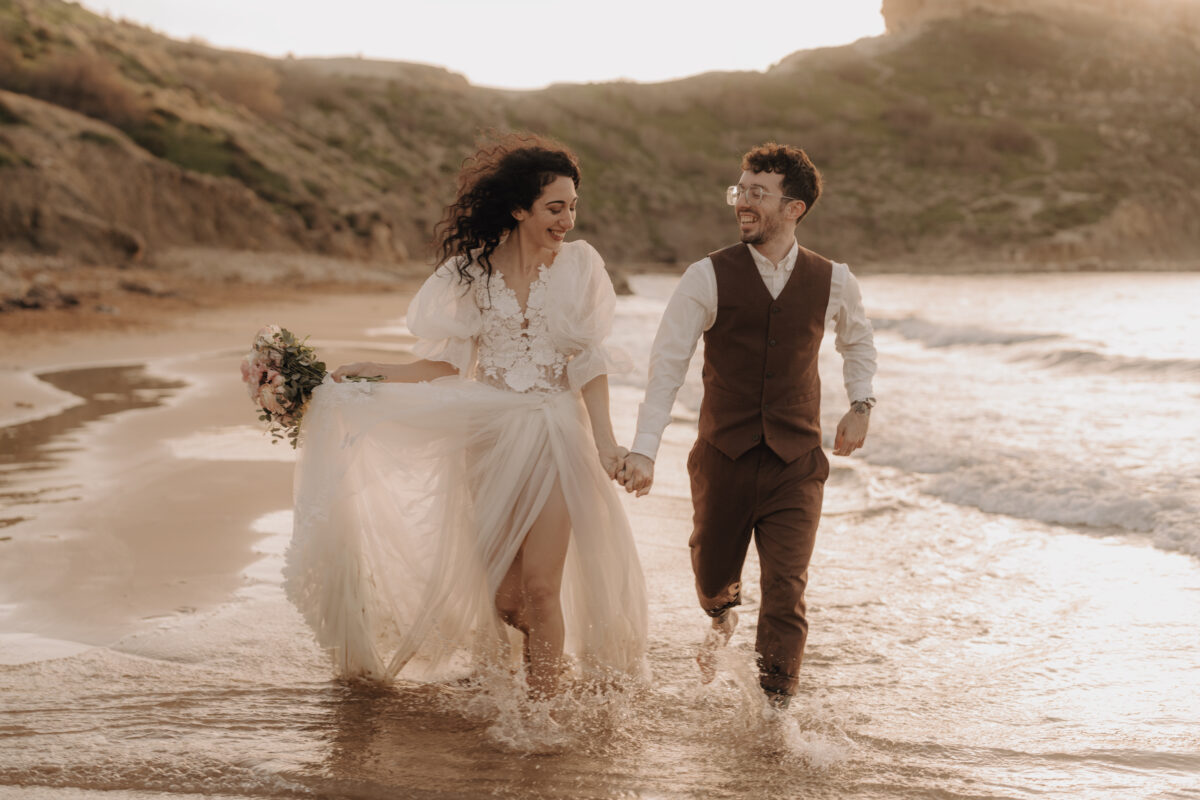 After Wedding Portfolio, Braut und Bräutigam laufen Hand in Hand durch das Meer an einem Strand und schauen sich an