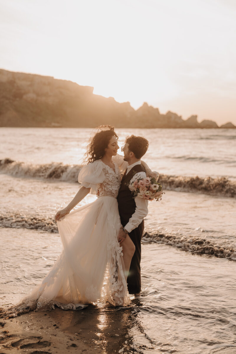 After Wedding Portfolio, Bräutigam hält seine Braut eng an sich gedrückt, sie stehen im Meer an einem Strand bei untergehender Sonne