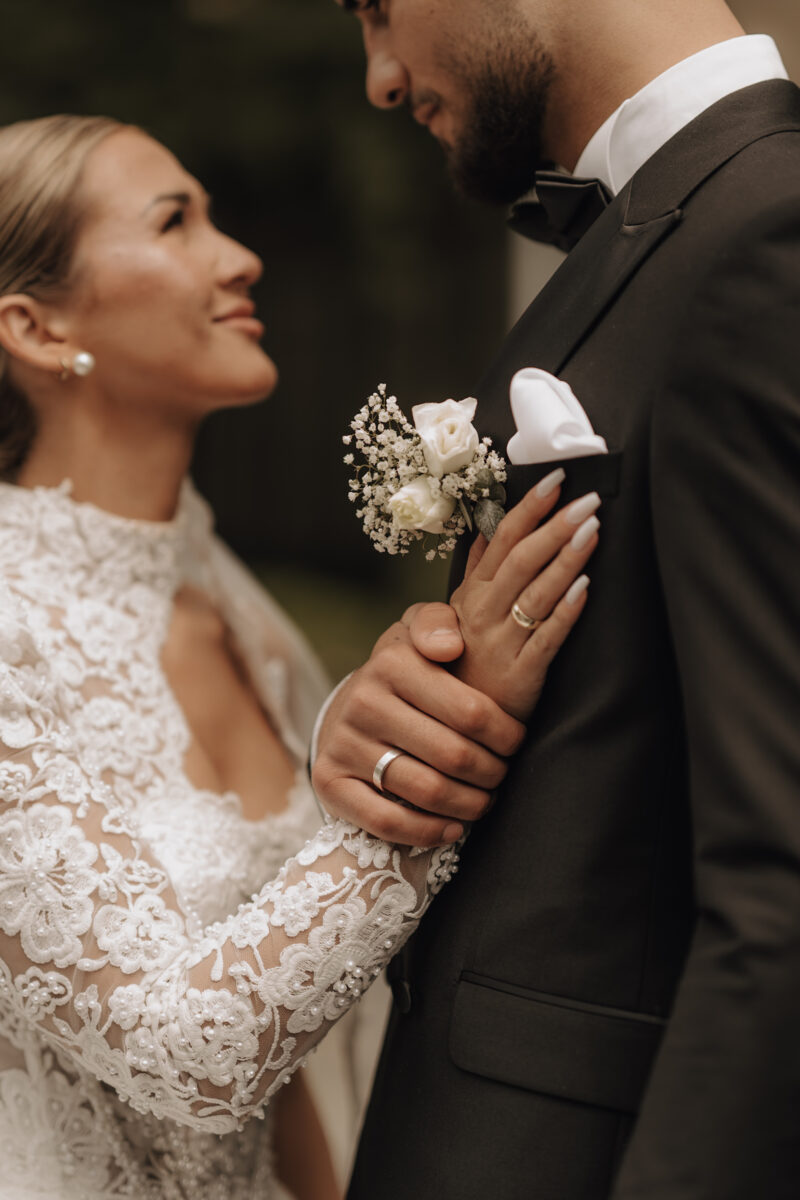 After Wedding Portfolio, Detailfoto der Eheringe, Hand der Braut liegt auf dem Jacket ihres Mannes und seine Hand auf ihrer, sie sehen sich dabei verliebt in die Augen