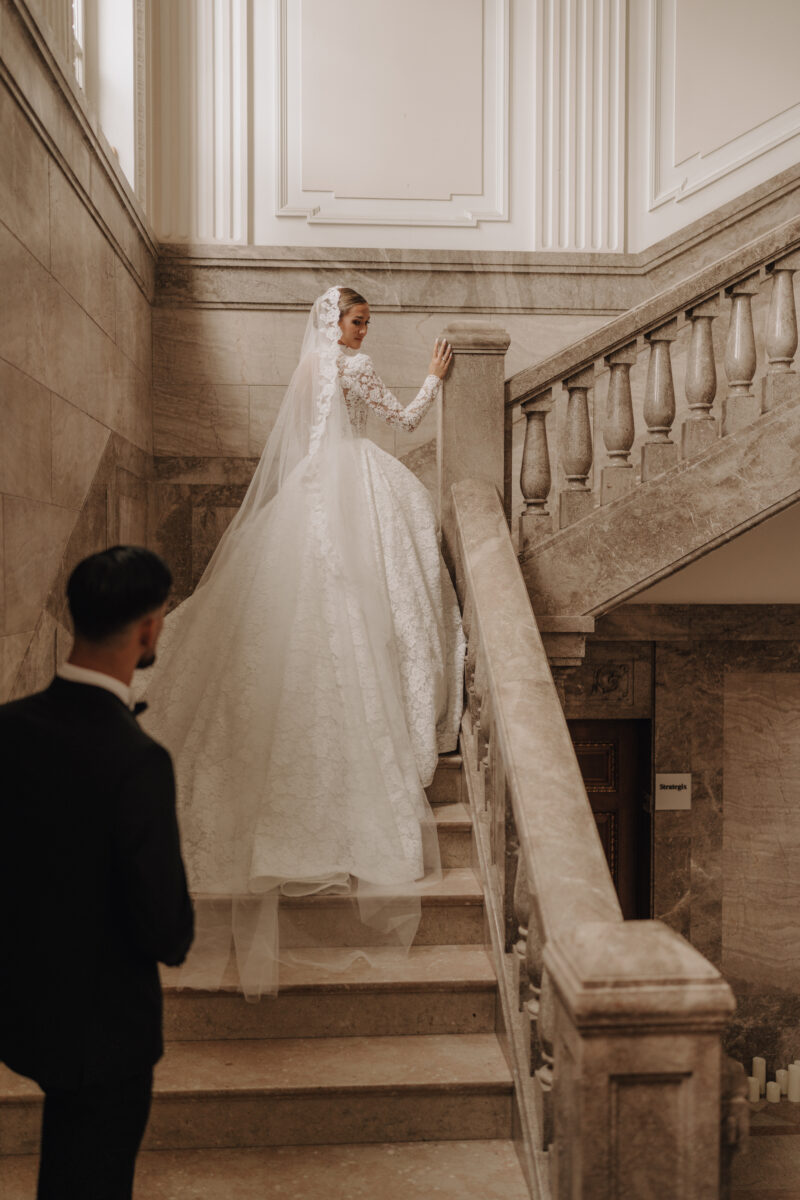 After Wedding Portfolio, Braut läuft eine Treppe im Schloss hinauf und schaut zurück, Bräutigam folgt ihr