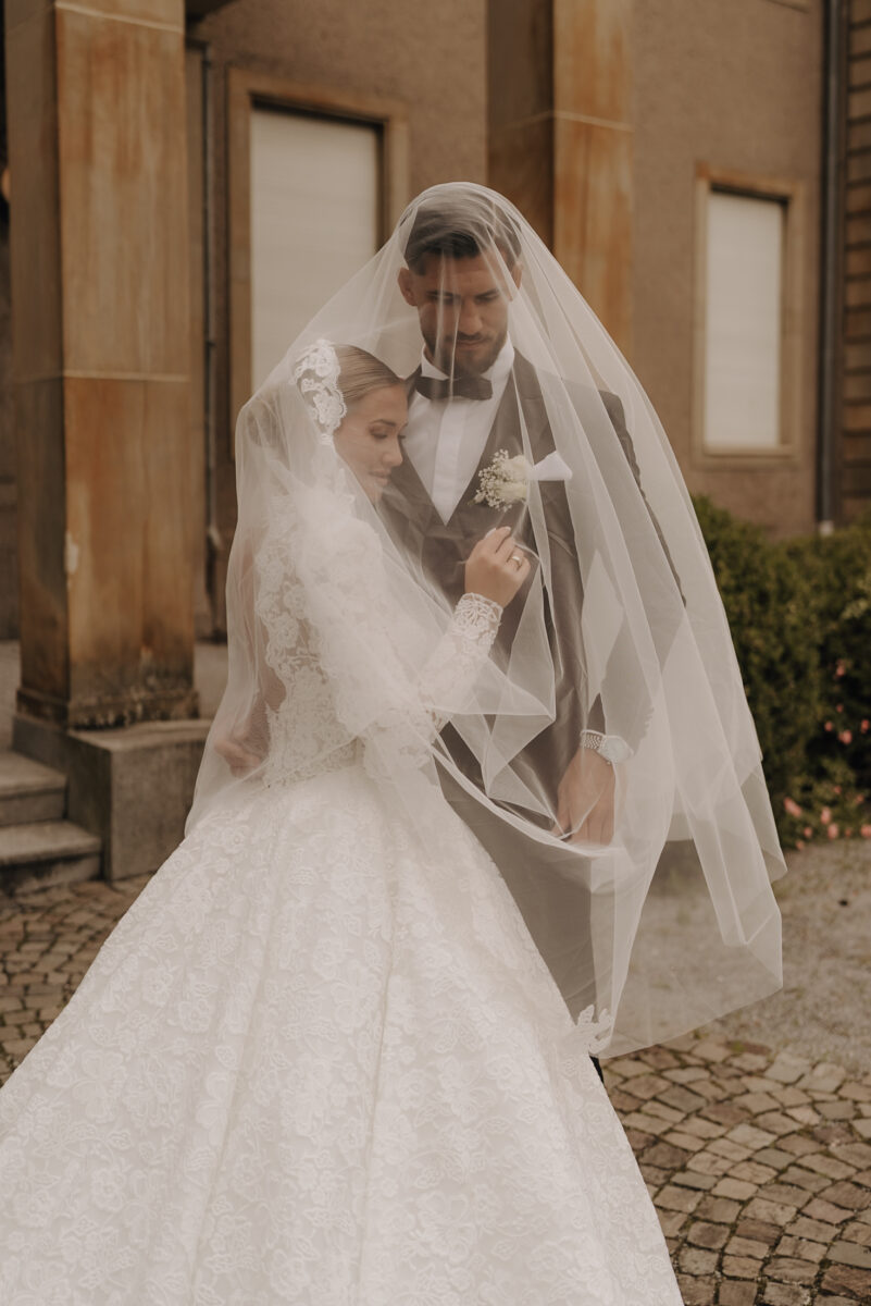 After Wedding Portfolio, Bräutigam hält Braut in den Armen und beide schauen Richtung Boden, sie sind von dem Schleier bedeckt