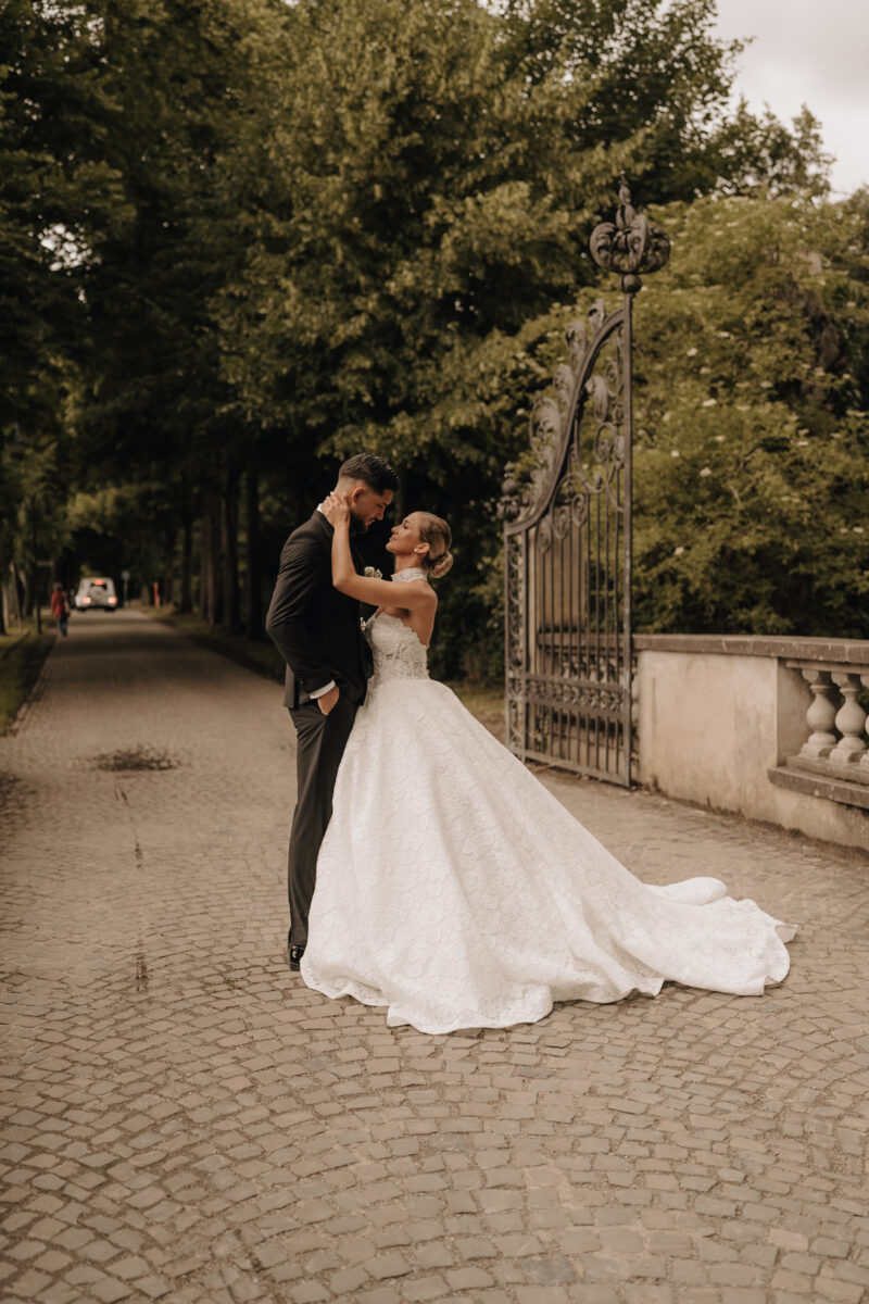 After Wedding Portfolio, Braut und Bräutigam stehen in einer Allee aus Bäumen und sehen sich in die Augen