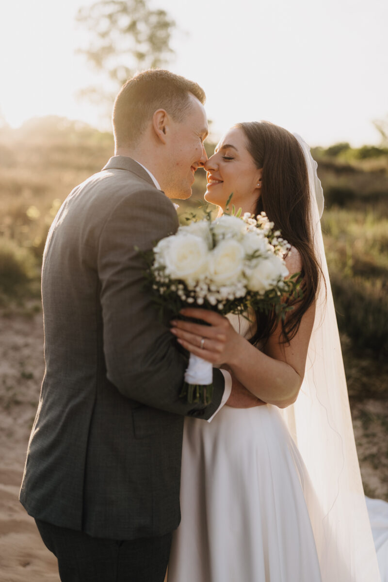 After Wedding Portfolio, Braut und Bräutigam stehen voreinander und ihre Nasenspitzen berühren sich, im Hintergrund geht die Sonne über der Heide unter