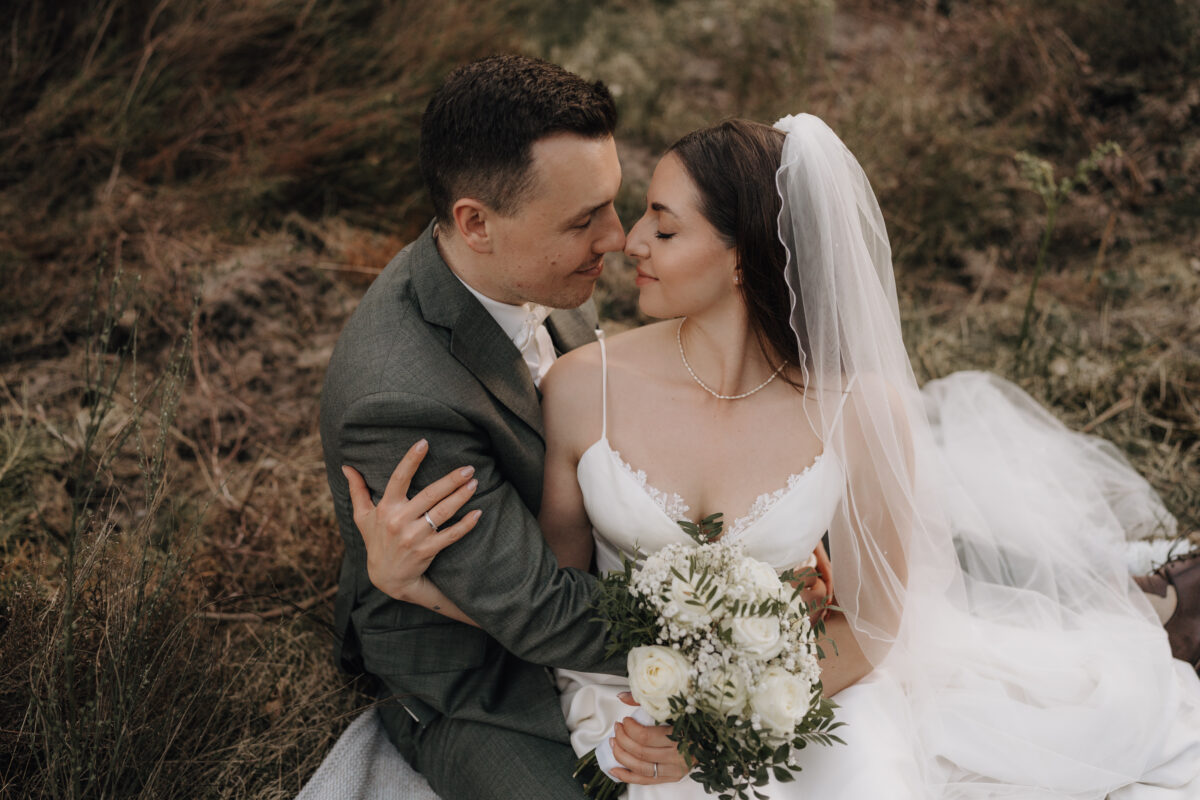 After Wedding Portfolio, Braut sitzt auf dem Schoß des Bräutigams in seinen Armen und sie haben ihre Nasenspitzen aneinander